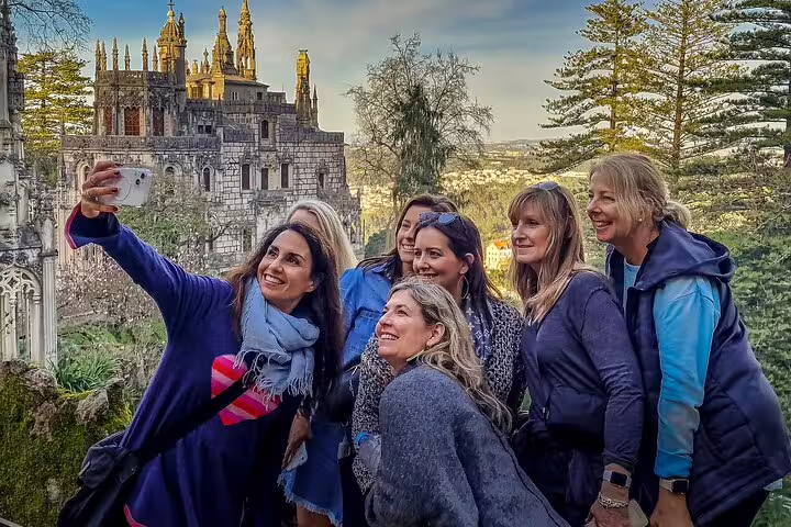 Group of tourists taking a selfie with the stunning architecture of Sintra's monuments in the background during a private tour from Lisbon.