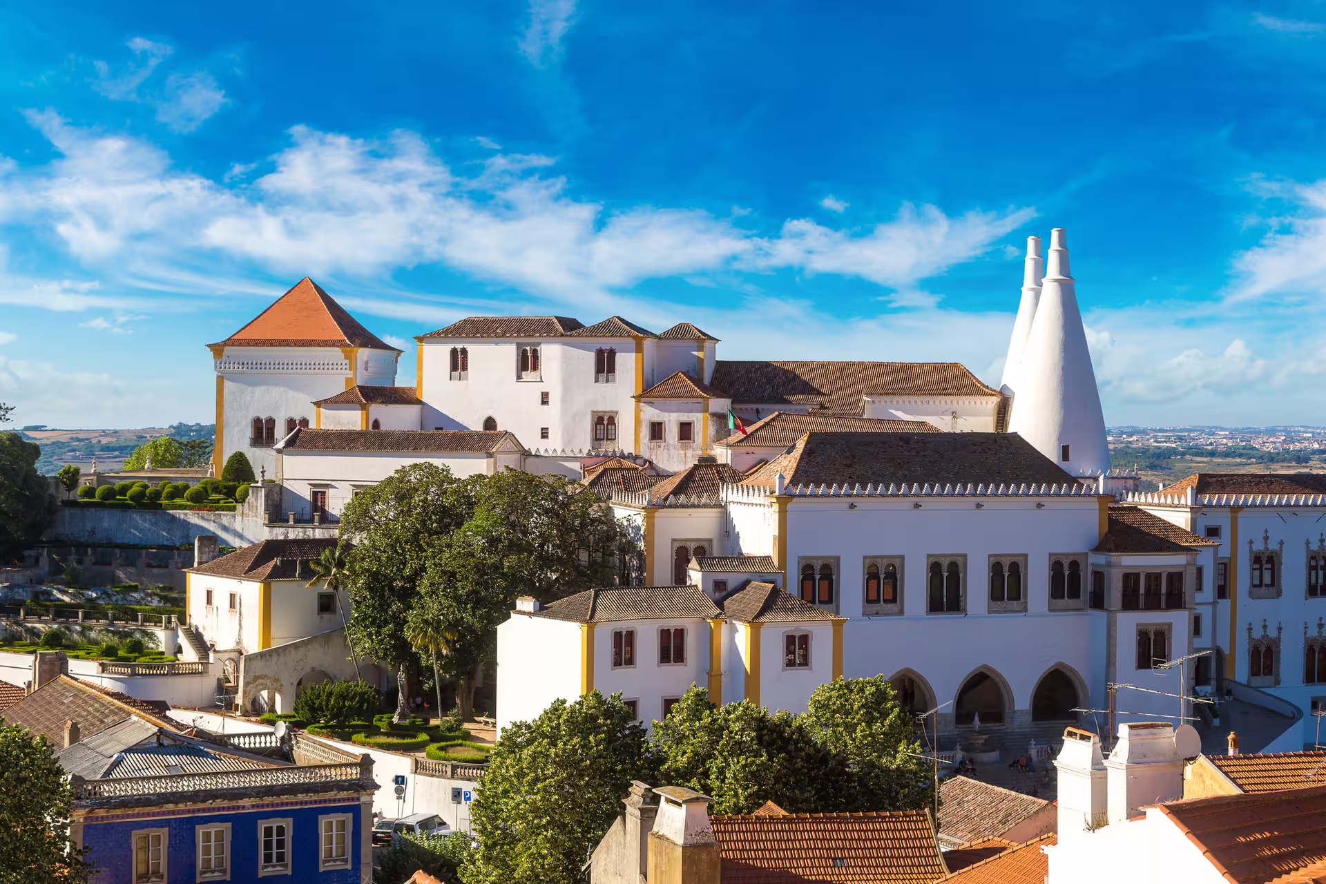 Scenic view of Sintra National Palace under a bright blue sky, featured in Lisbon shore excursion with tram and Pena Palace tickets.