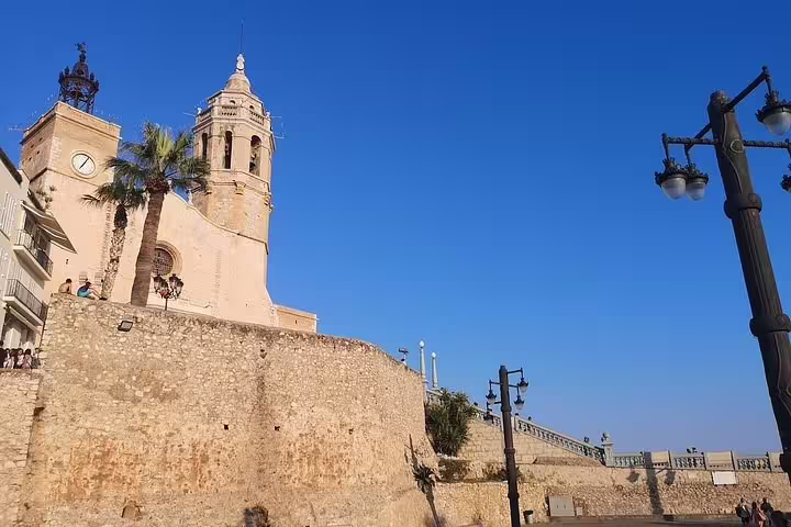 Historic church and stone walls under a clear blue sky in Sitges, featured on the Wine Celler Penedés tour.