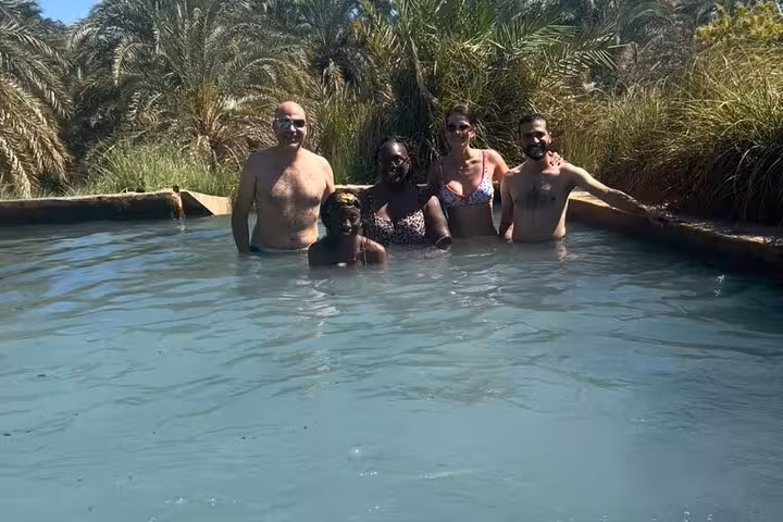 Group relaxing in Siwa Oasis hot spring pool, a refreshing stop on 3-day White Desert camping safari
