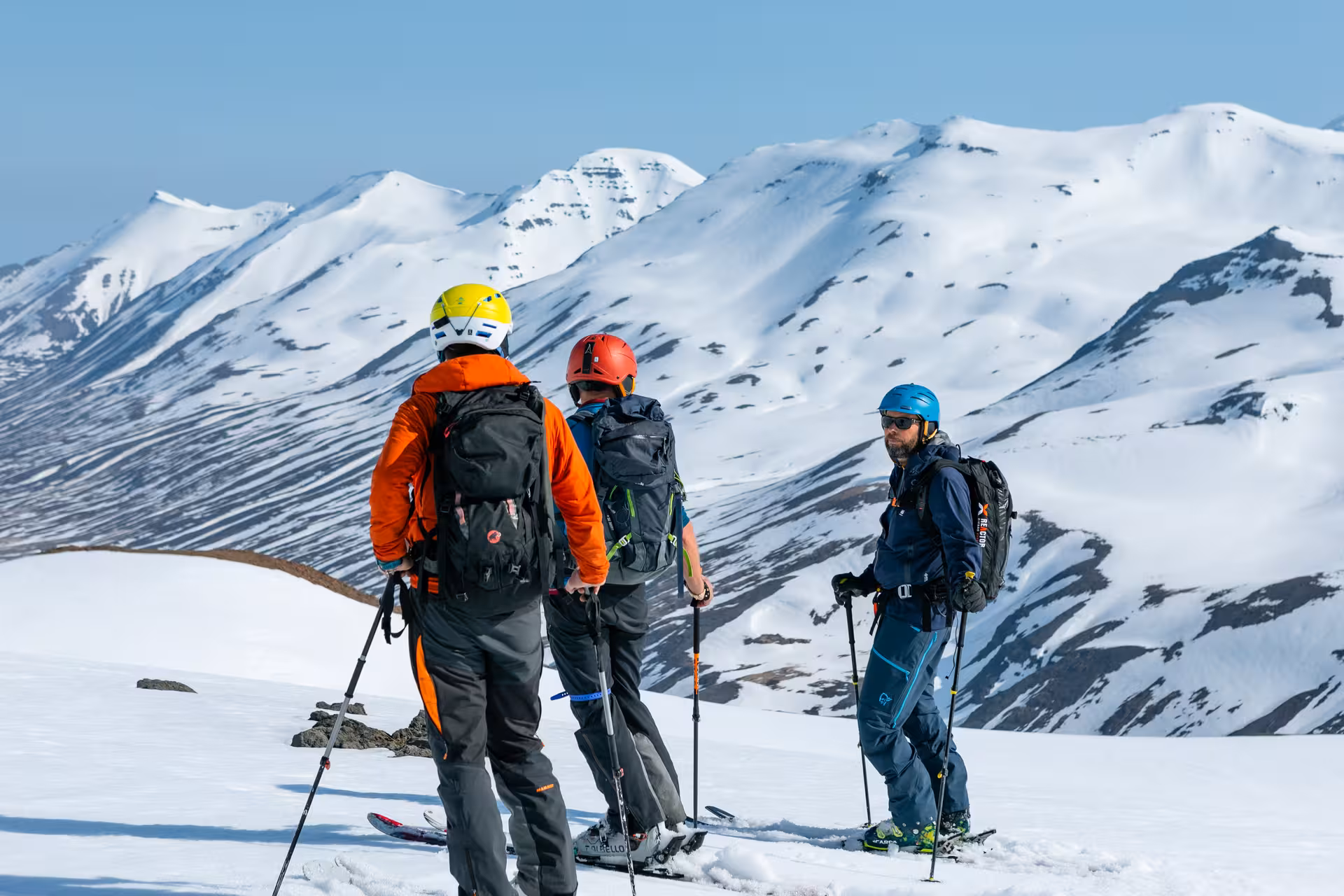 Group of skiers in colorful helmets admire breathtaking snowy mountain vistas on heli-touring getaway.