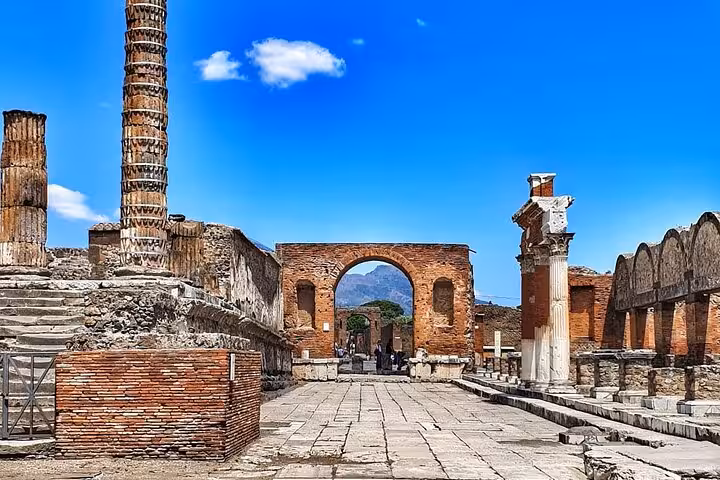 Explore ancient ruins with stunning columns and arches on a skip-the-line Pompeii guided tour under a clear blue sky.