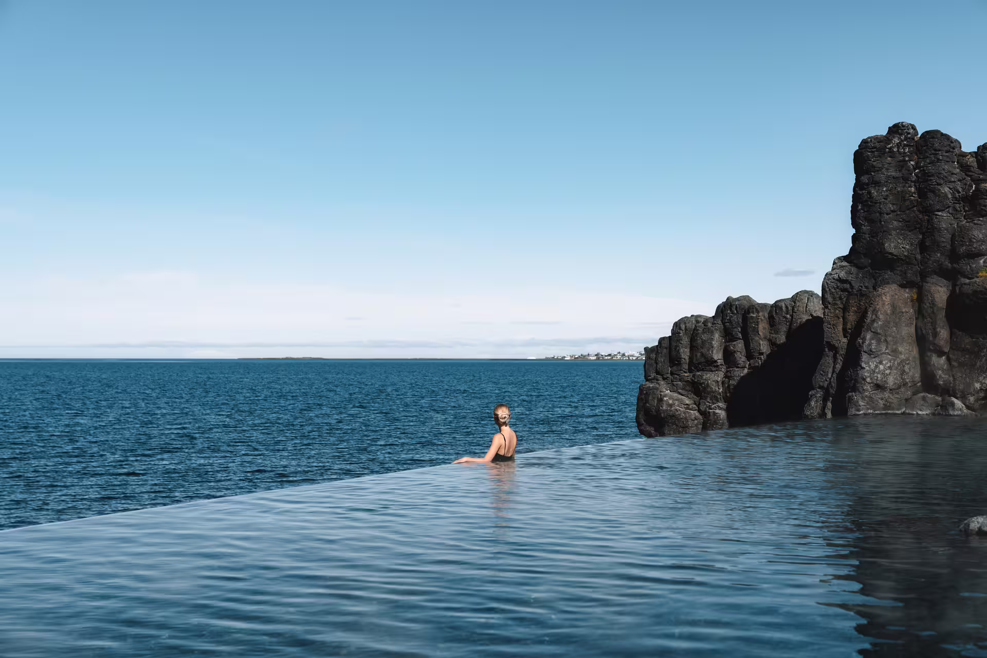 Person relaxing in the serene, geothermal waters of Sky Lagoon with stunning ocean views, part of the Golden Circle tour in Iceland.