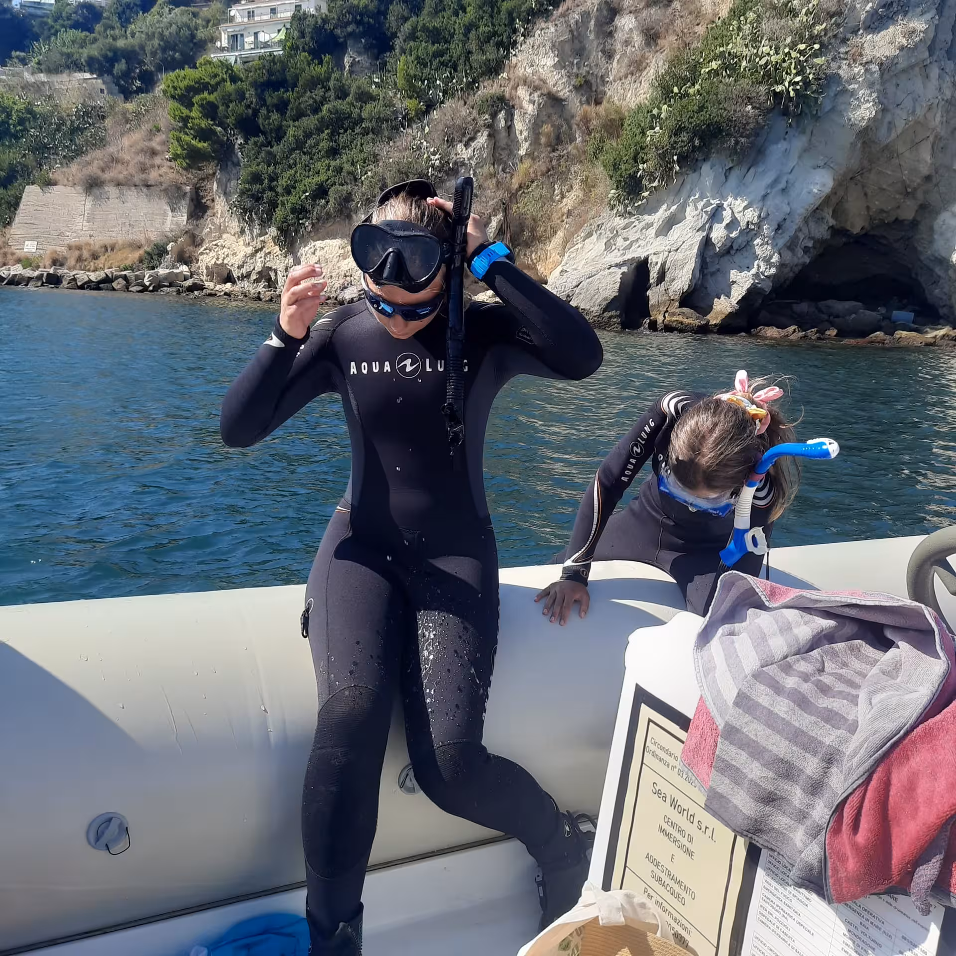 Two snorkelers on the side of the boat getting ready to enter the water, all dressed up in their suits.