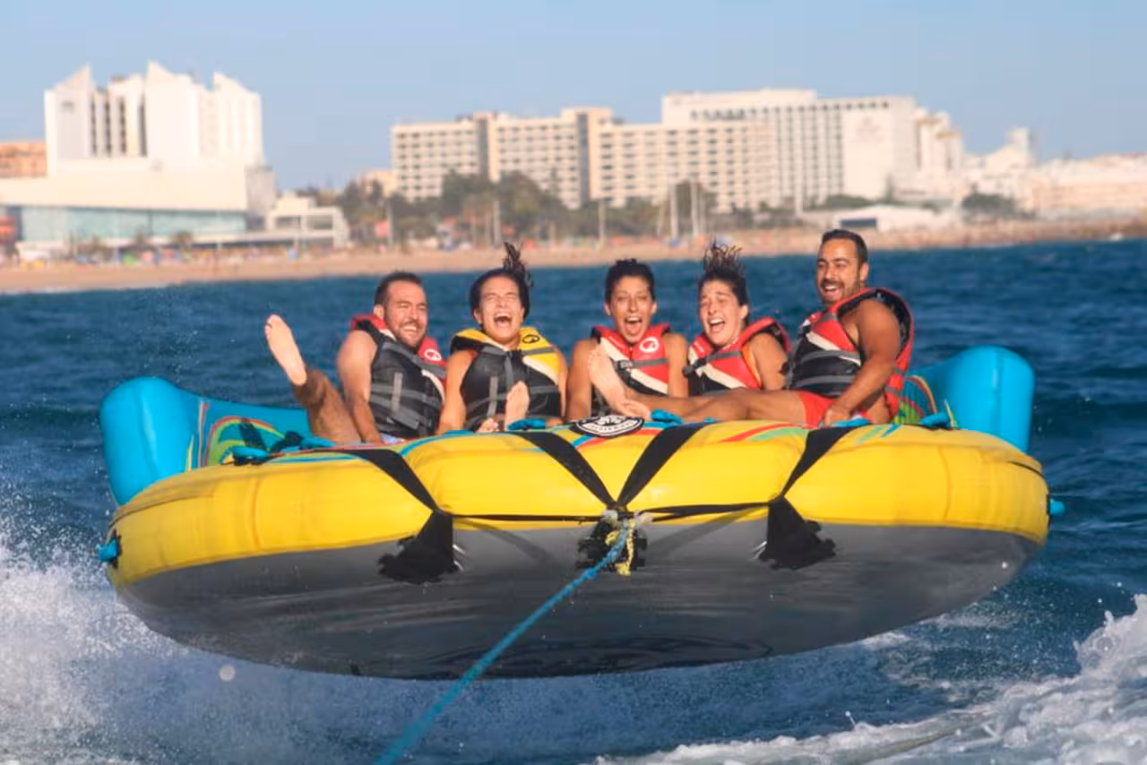 Group of friends on Sonar inflatable tube ride, flying over blue sea on a thrilling beach holiday water sports tour