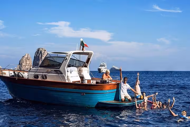 Tourists enjoying a swim near a boat on the stunning Sorrento Coast with vibrant blue waters and iconic rocks.