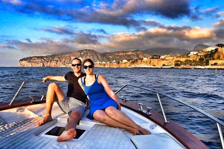 Couple relaxing on a boat with stunning views of the Sorrento Coast at sunset.