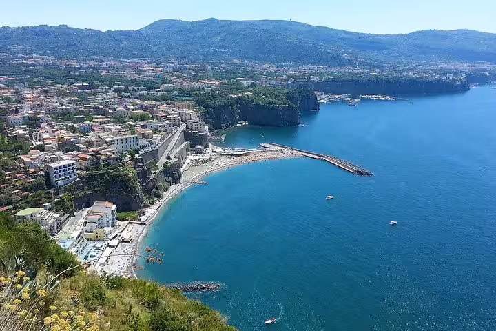 Aerial view of Sorrento's stunning coastline with vibrant blue waters and lush green hills, perfect for a day trip.
