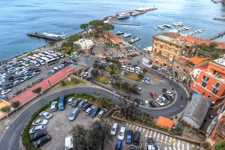 Aerial view of Sorrento's scenic coastline with winding roads, vibrant buildings, and bustling harbor, ideal for tours.