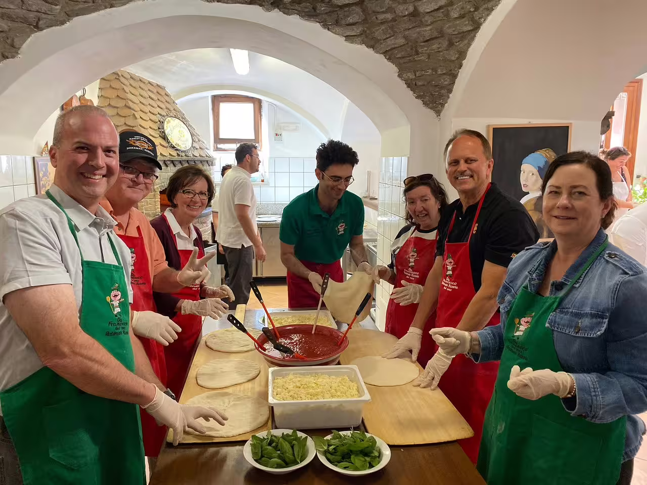 Happy travelers in aprons making Neapolitan pizza during a hands-on cooking class on a weekend farm tour in Sorrento, Italy