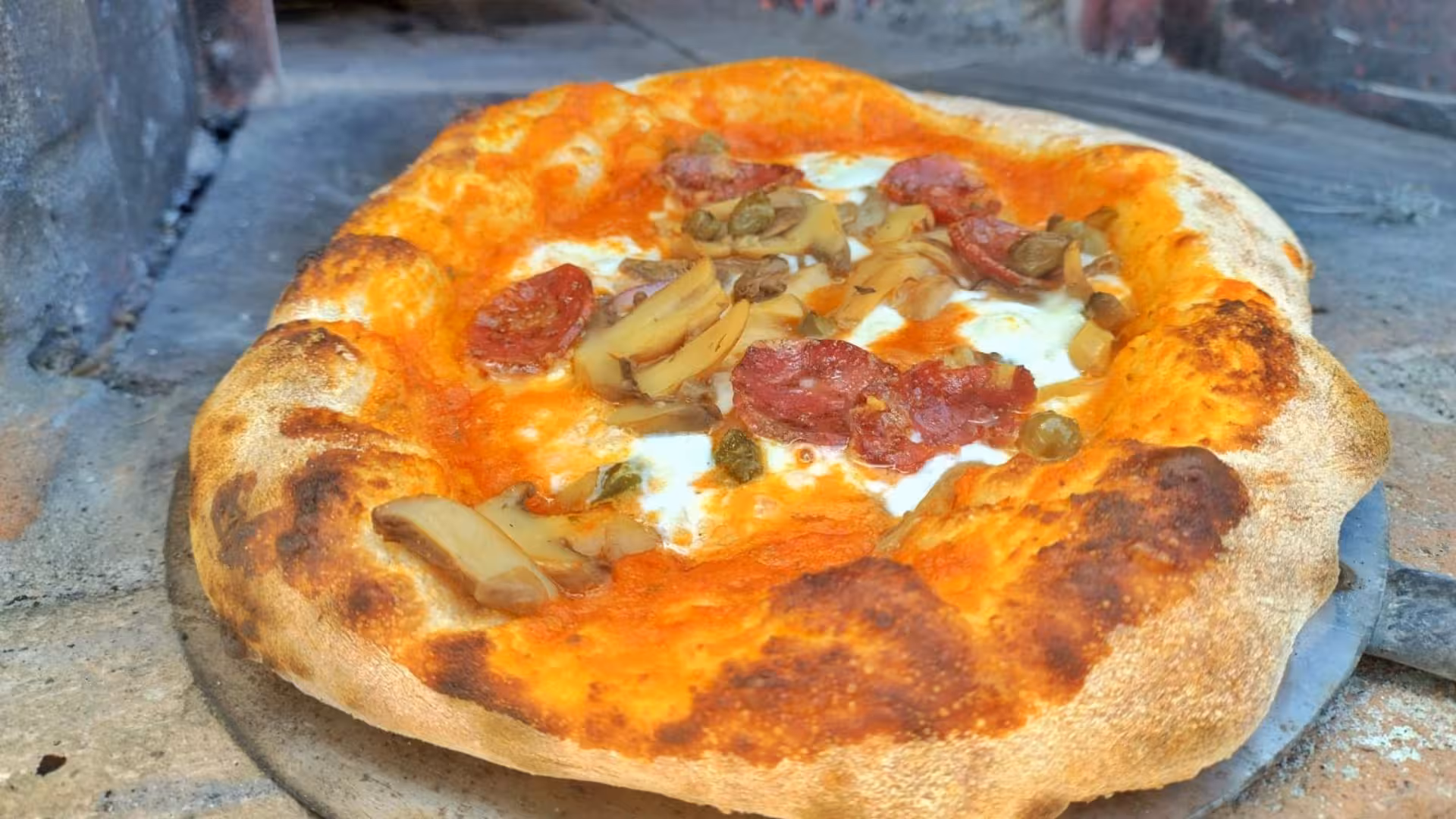 Freshly baked pizza with mushrooms and pepperoni from a traditional wood-fired oven at Sorso villa workshop.