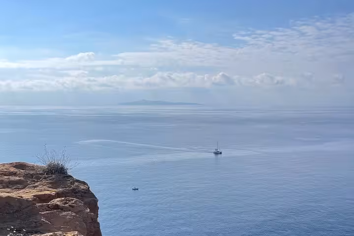 Scenic view of the Aegean Sea from Sounio, featuring a distant sailboat under a bright blue sky.