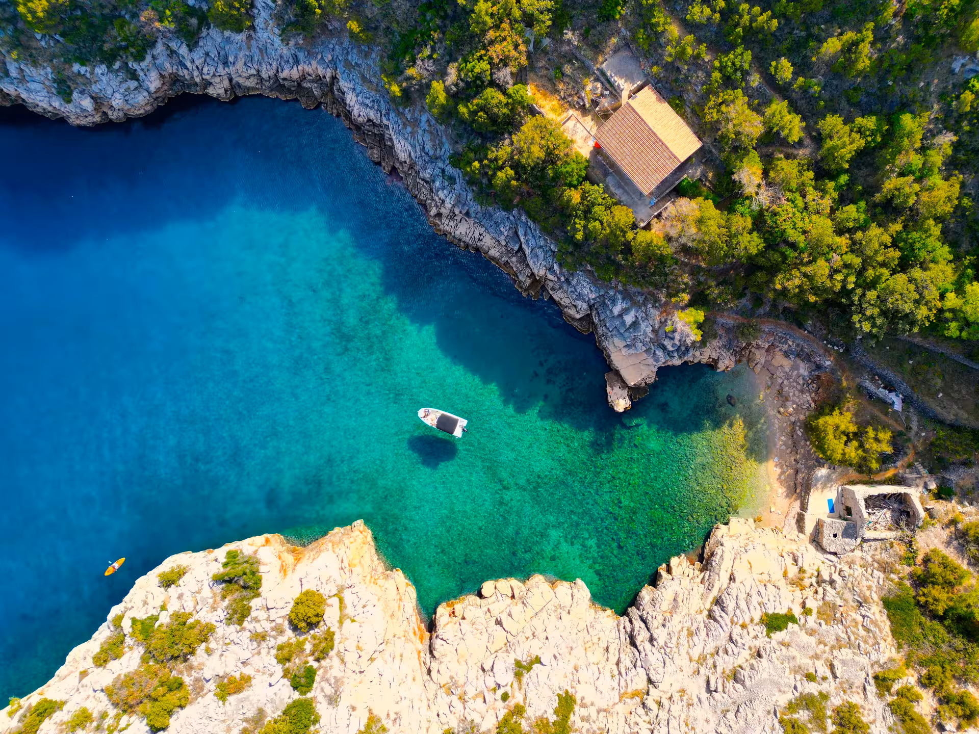 Aerial view of speedboat in turquoise Blue Lagoon cove on 3 Islands tour, rocky cliffs and pine forest