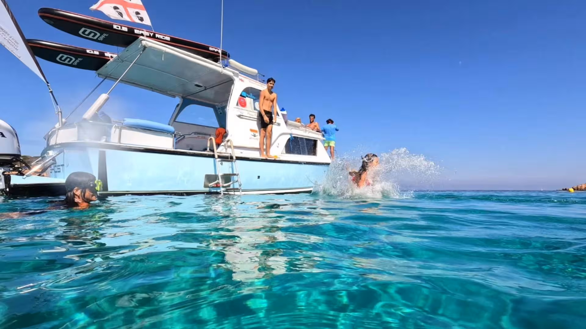 People enjoying a swim and diving off a speedboat in the crystal-clear waters of La Maddalena Archipelago.