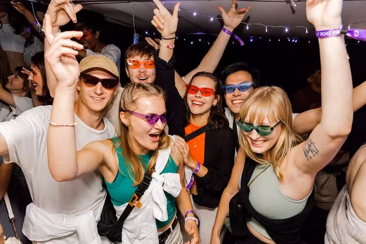 Excited partygoers wearing colorful sunglasses dancing on the Split After Dark boat crawl experience.
