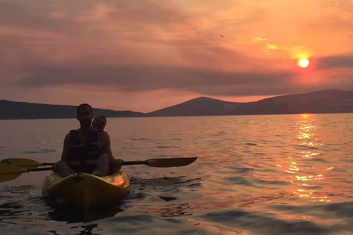 Couple sea kayaking at sunset near Split, Croatia, on a guided tour with wine, golden Adriatic reflections