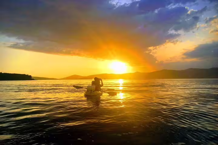 Couple sea kayaking at sunset near Split, Croatia, on an Adriatic tour with wine and golden reflections