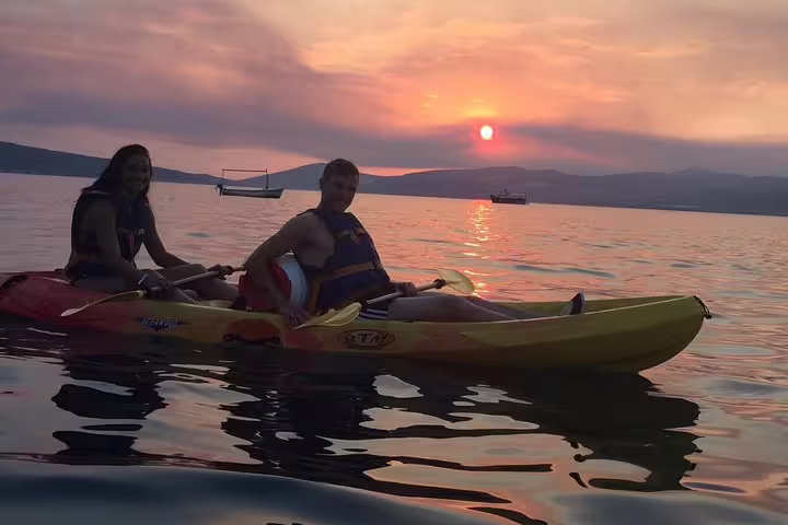 Two kayakers in tandem at Split sunset, calm Adriatic sea with boats in distance on wine kayaking tour