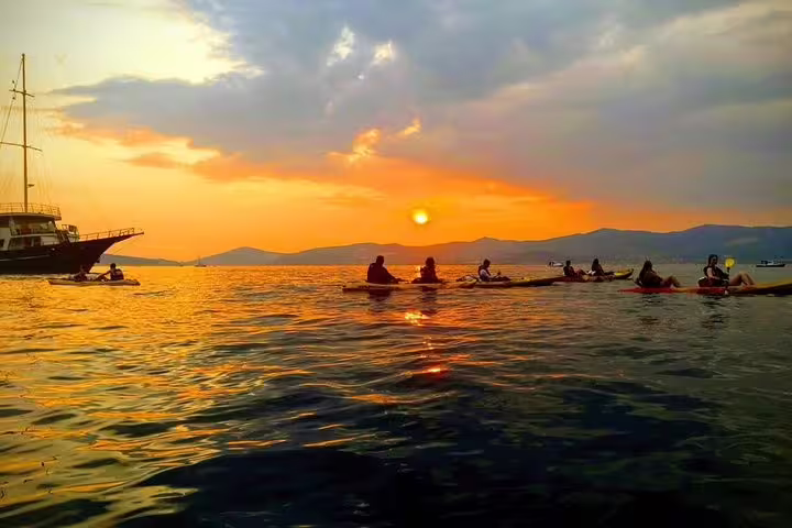 Group sea kayaking at sunset in Split, Croatia, with a sailboat nearby on an Adriatic wine tasting tour