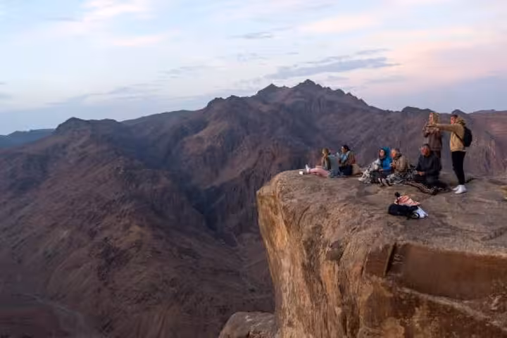 Travelers rest on Mount Sinai summit cliff at dawn on St Catherine’s Monastery tour from Sharm El Sheikh