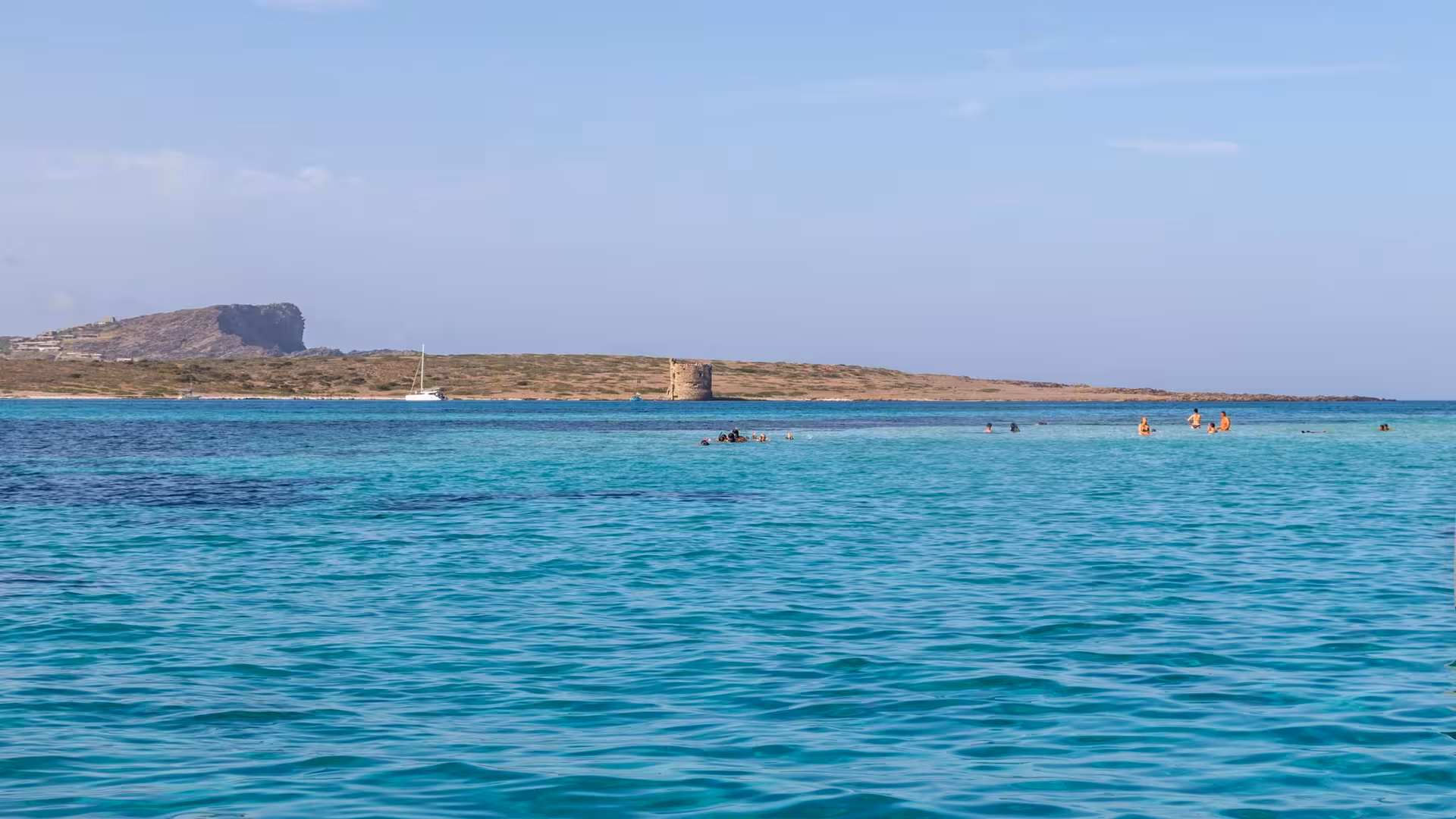 Scenic view of Asinara Island with swimmers and a sailboat, captured during a Stintino catamaran tour.