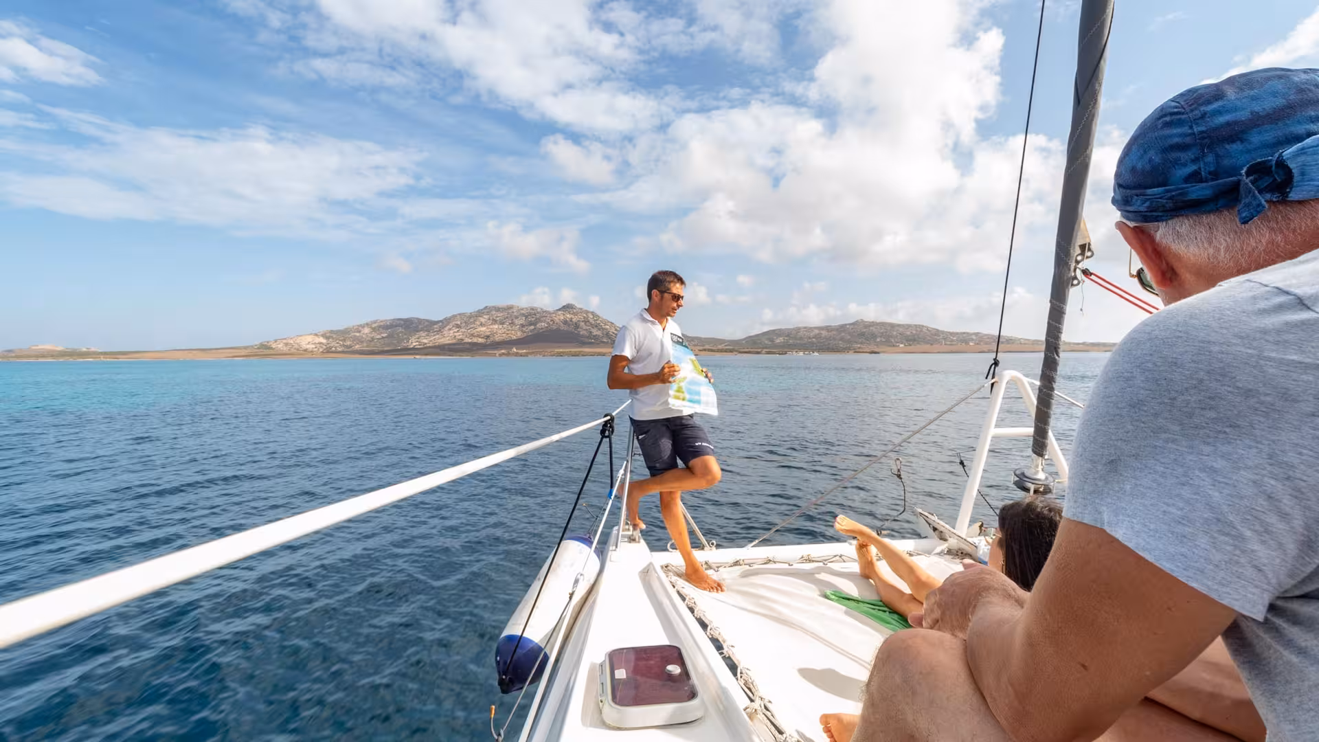 Tourists relax on a catamaran deck enjoying a scenic journey to Asinara Island under a bright blue sky.