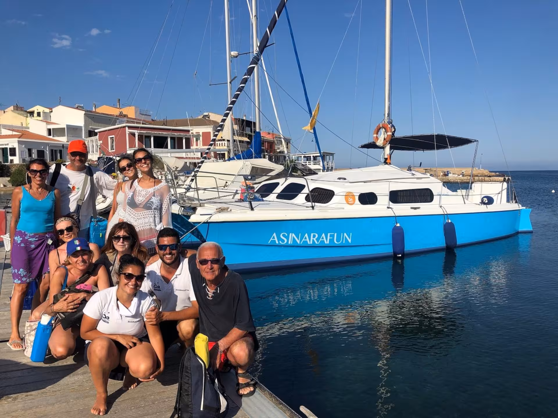 Group of tourists posing by a docked catamaran in Stintino, ready for an adventure in the Gulf of Asinara under a sunny sky.