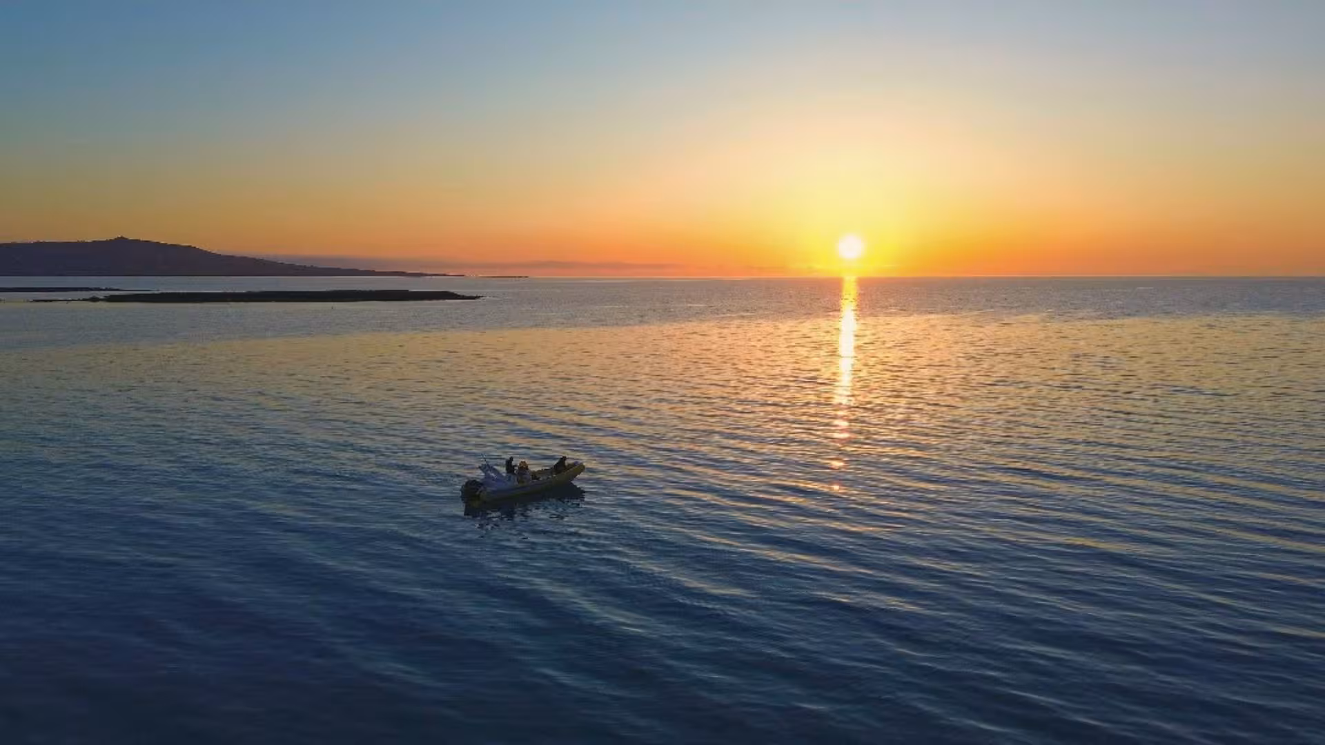 A serene dinghy tour from Stintino at sunrise with a vibrant sky reflecting on calm Mediterranean waters.