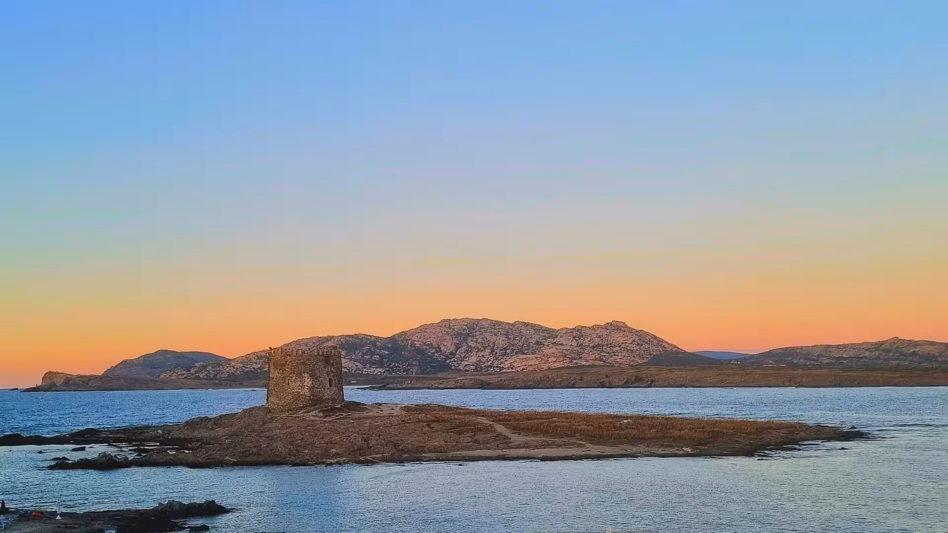 Historic coastal tower on a rocky islet bathed in soft sunset hues during a Stintino dinghy tour.