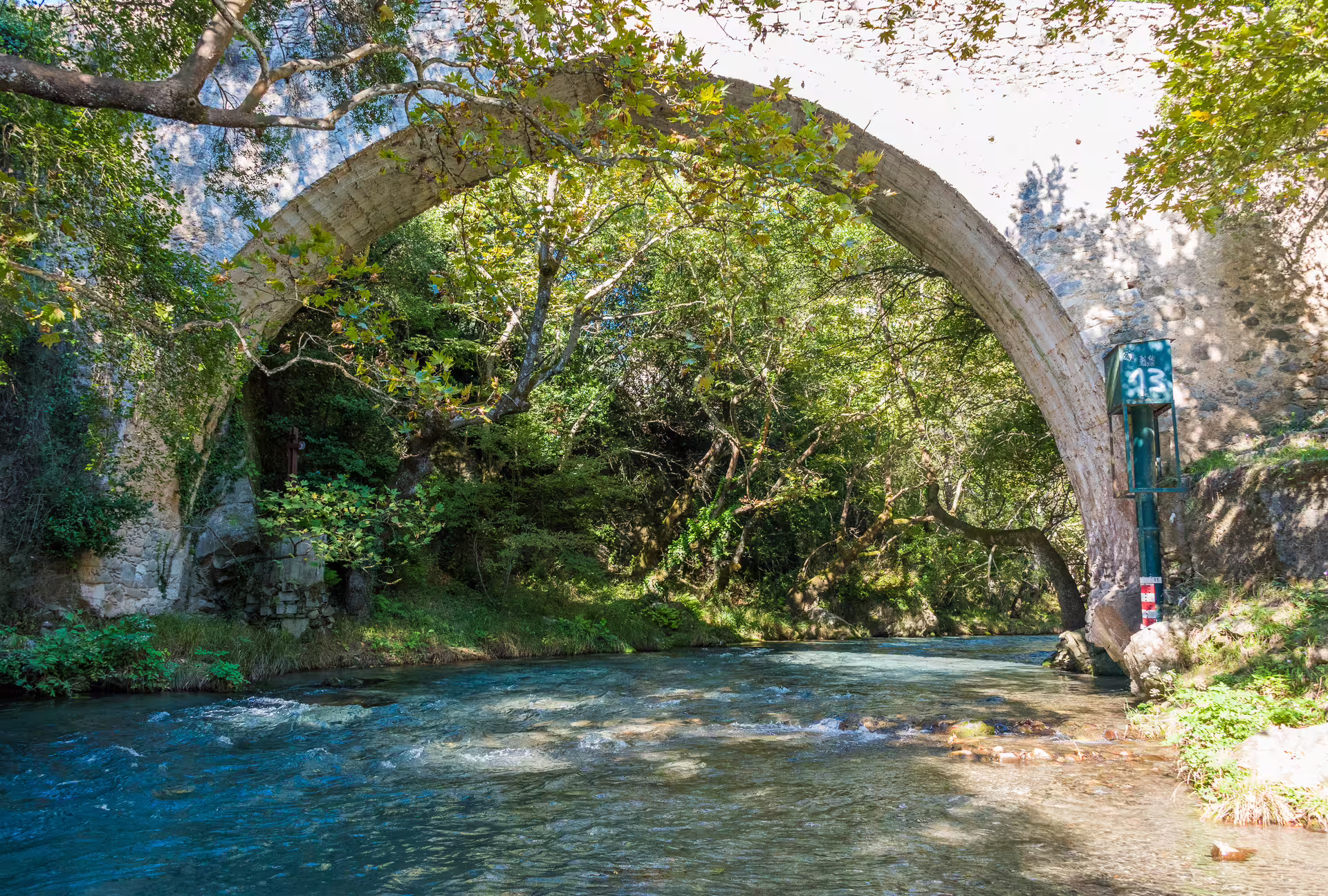 Stone arch bridge over the Lousios River in shaded gorge forest, Peloponnese, on a scenic hiking tour