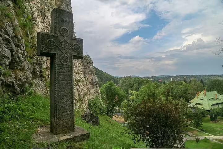 Ancient carved stone cross monument beside rocky cliff overlooking forested valley near Bran Castle, Brasov