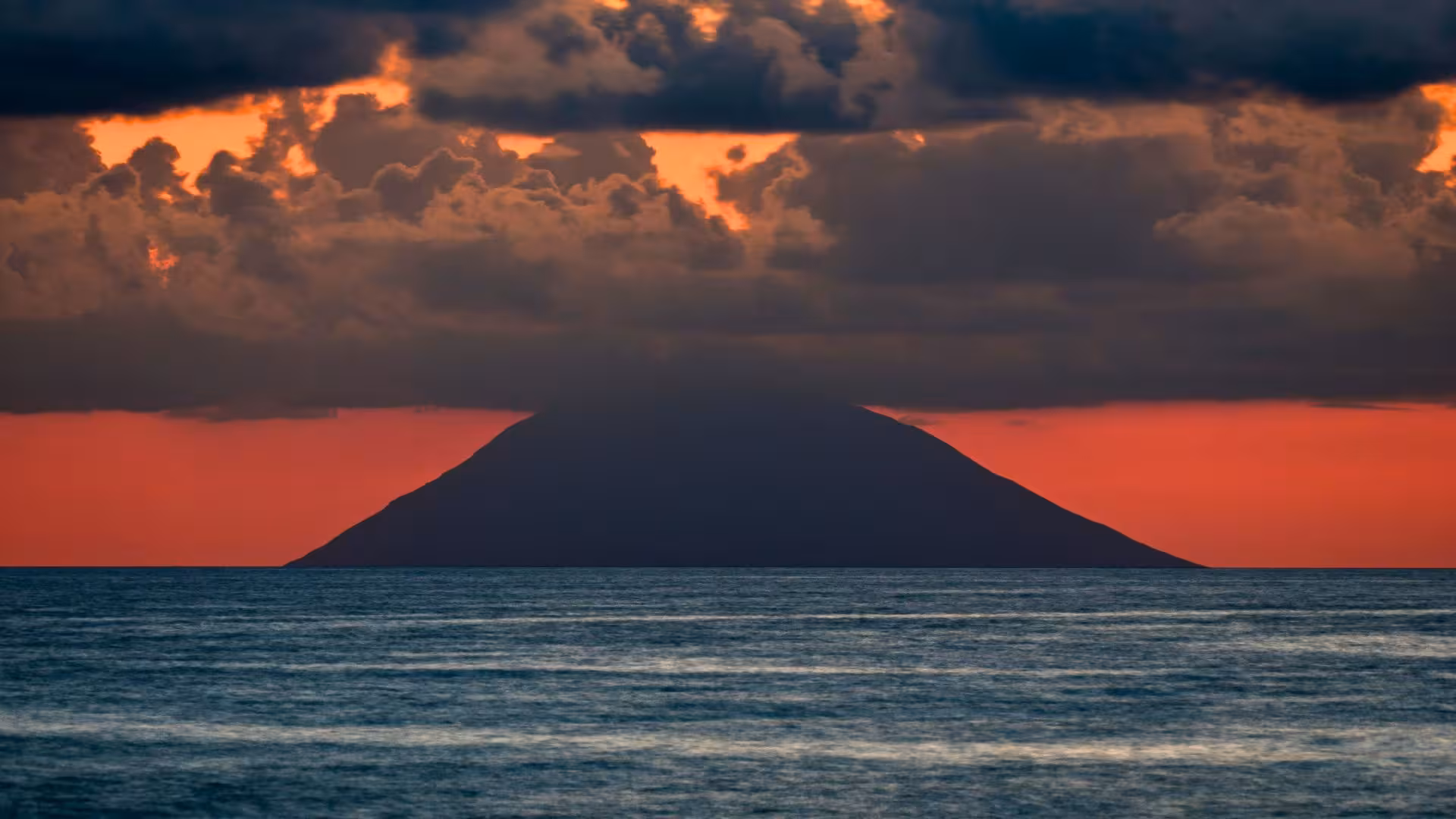 Dramatic sunset over the sea with silhouette of Stromboli volcano, ideal for Aeolian Islands motorboat excursions.