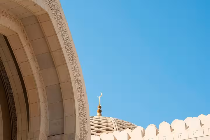 Ornate arch and domed roof of Sultan Qaboos Grand Mosque against clear blue sky on Muscat classic private taxi tour