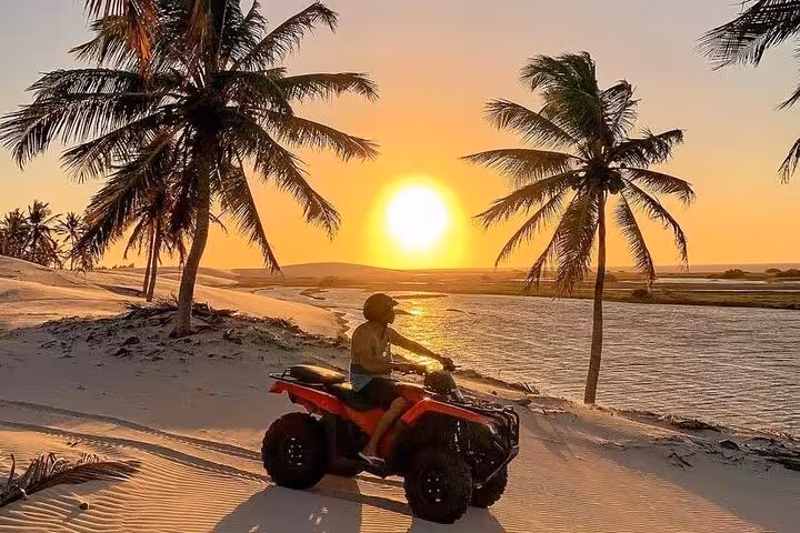 ATV rider at sunset in Jericoacoara dunes by a lagoon and palm trees, golden hour quad tour in Brazil