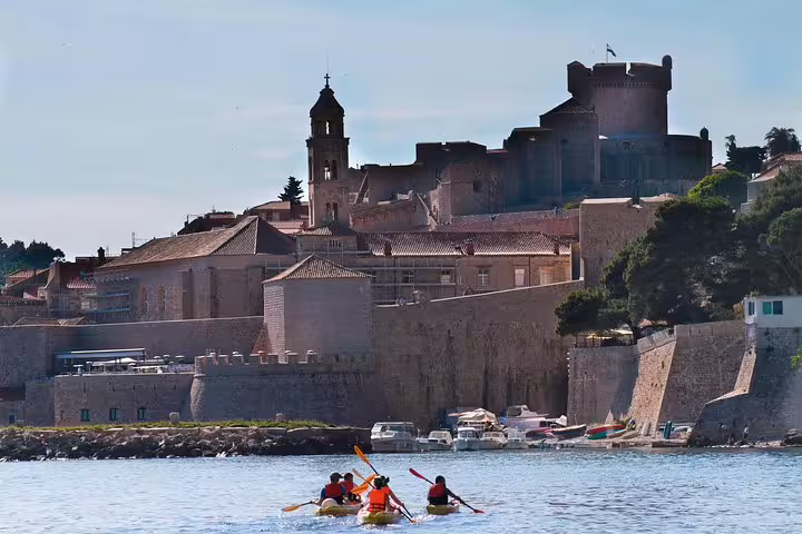 Kayakers paddling by Dubrovnik city walls and fort at dusk, snorkeling break with water and wine on tour