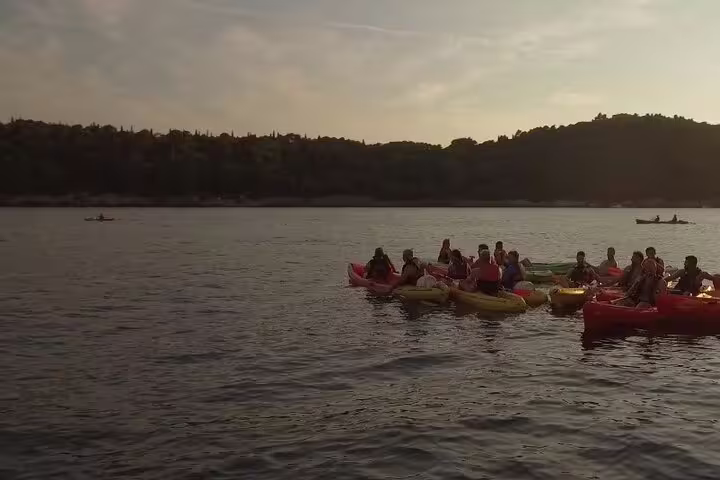 Group sunset kayaking on calm bay waters, part of guided snorkeling tour with water and wine on the sea