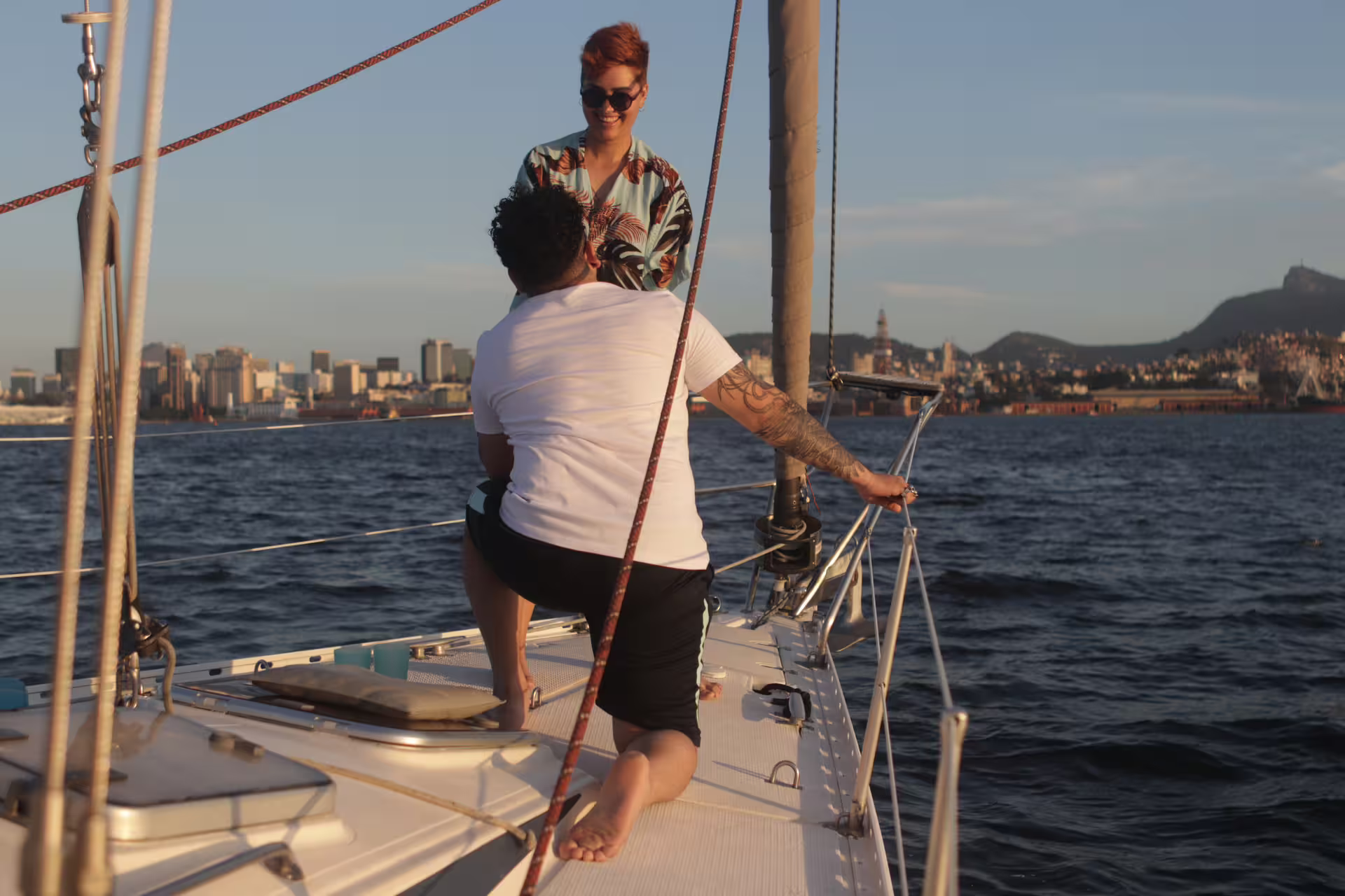 Romantic couple sharing a moment on a sailboat with Rio de Janeiro skyline at sunset.