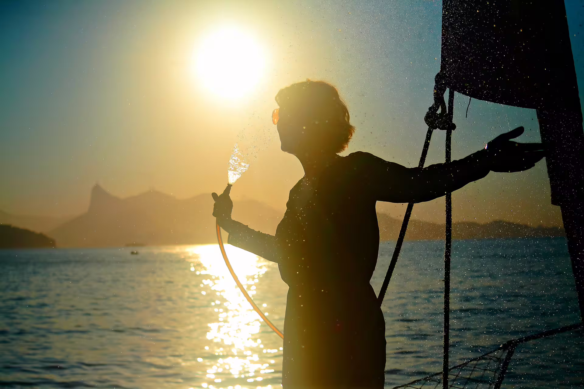 Silhouette of person enjoying sunset on a sailboat in Rio with sparkling water and scenic mountains.