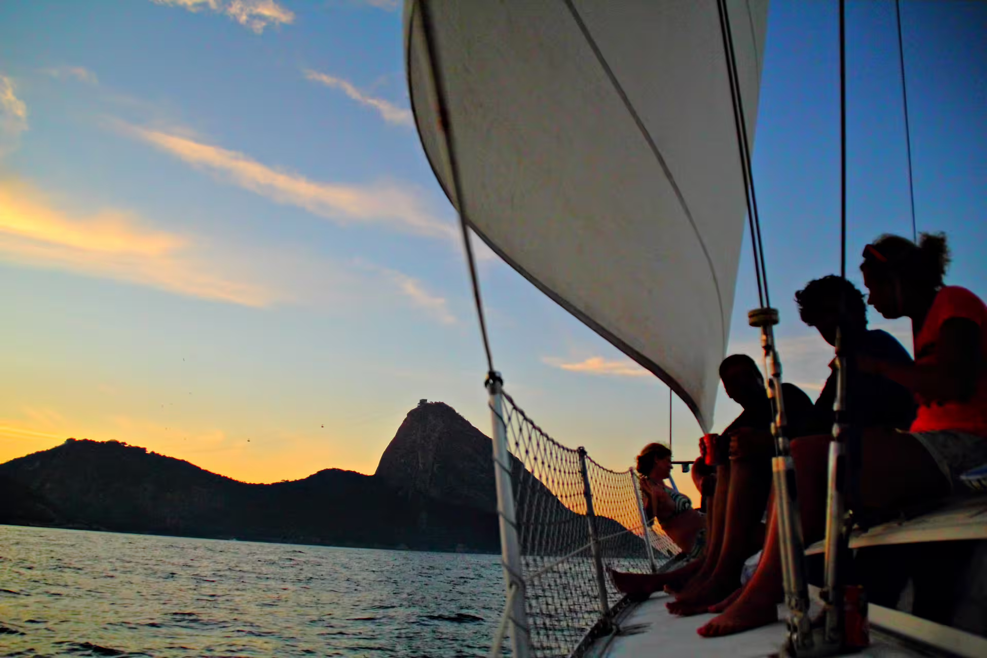 Group relaxing on sailboat at sunset with stunning view of Sugarloaf Mountain in Rio de Janeiro.