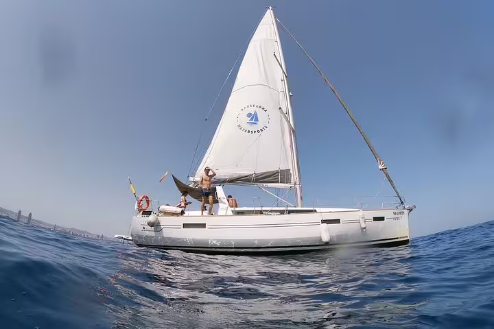 Sailboat gliding on clear blue waters during a 2-hour sunset sailing experience with open bar and tapas, perfect for relaxation.