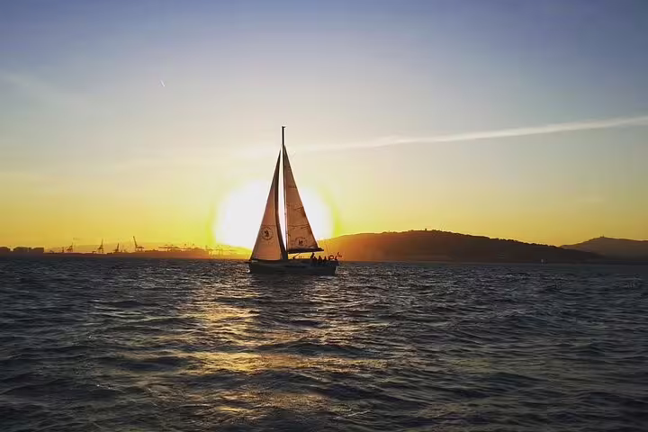 Sailboat gliding at sunset with open bar and tapas on a scenic 2-hour sailing experience, ideal for relaxation and sightseeing.