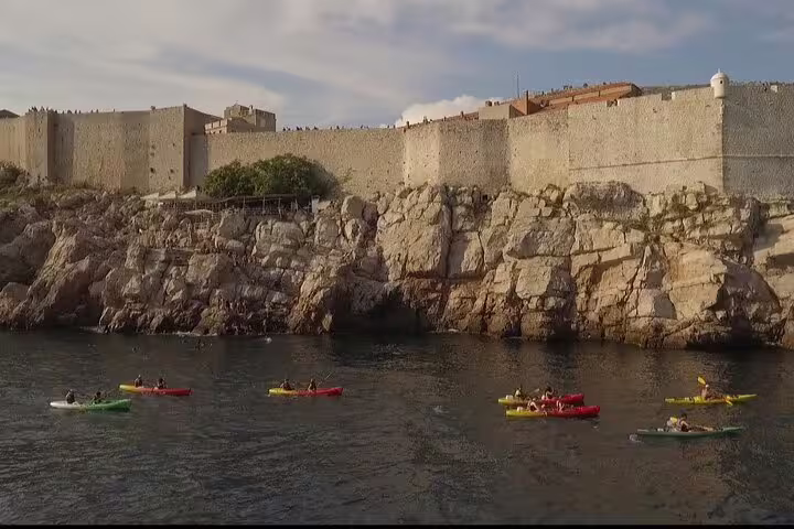 Group sea kayaking past coastal fortress walls at golden hour, part of sunset kayaking and snorkeling with wine tour