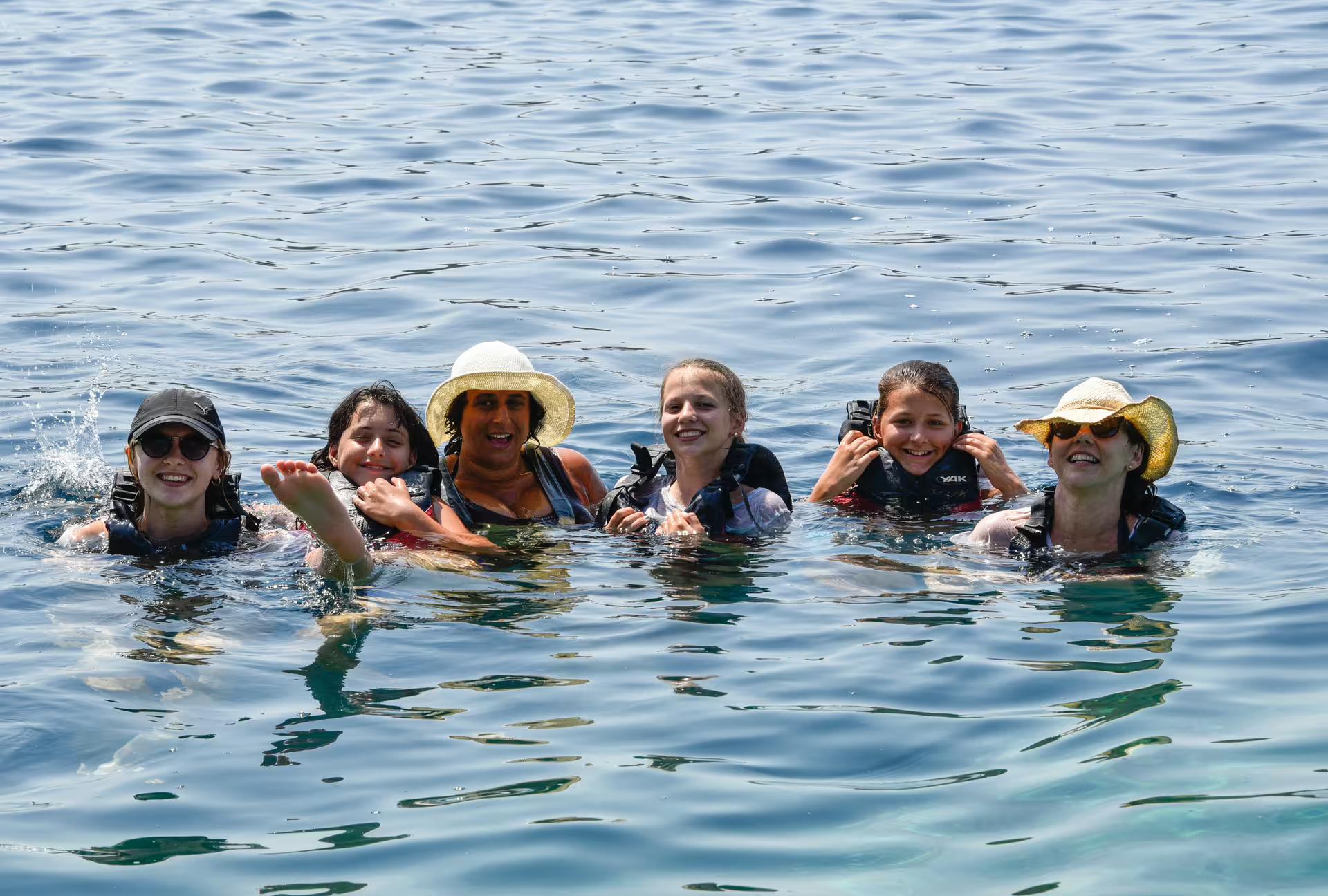 Smiling group floating in the sea on a SUP in Kardamyli break, Mani coast, with life vests and sun hats
