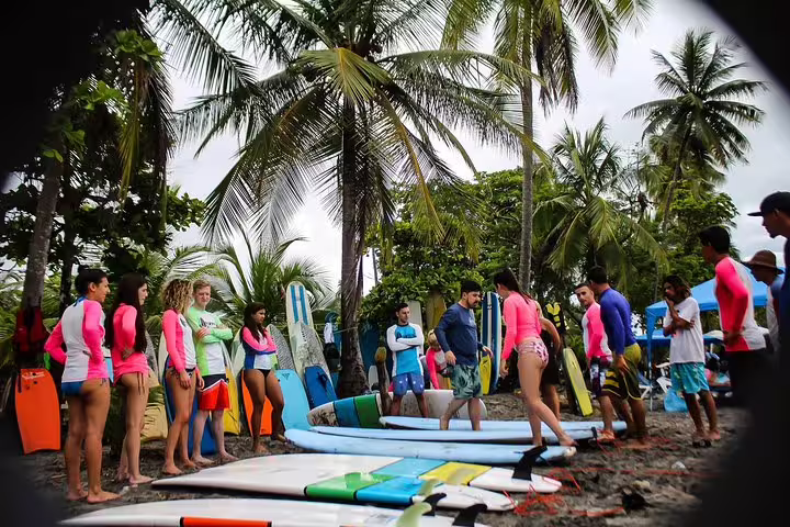 Surf instructor demonstrating techniques to eager students on a tropical Manuel Antonio beach, surrounded by surfboards.