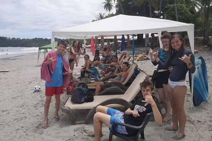 Group of happy tourists under a beach canopy, ready to enjoy surf lessons in picturesque Manuel Antonio.