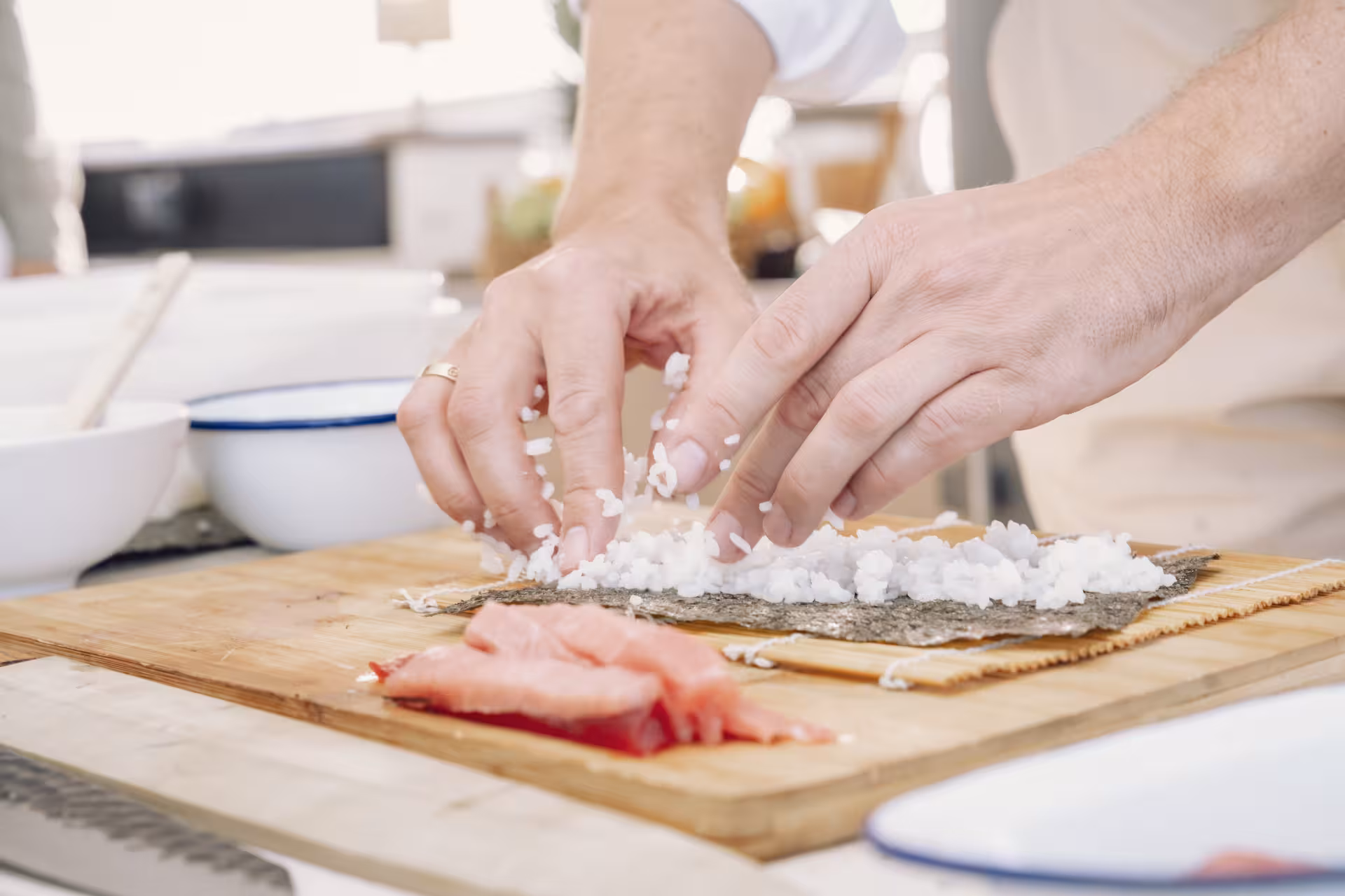 Hands spreading sushi rice on nori over bamboo mat in a sushi masterclass, learning maki roll techniques
