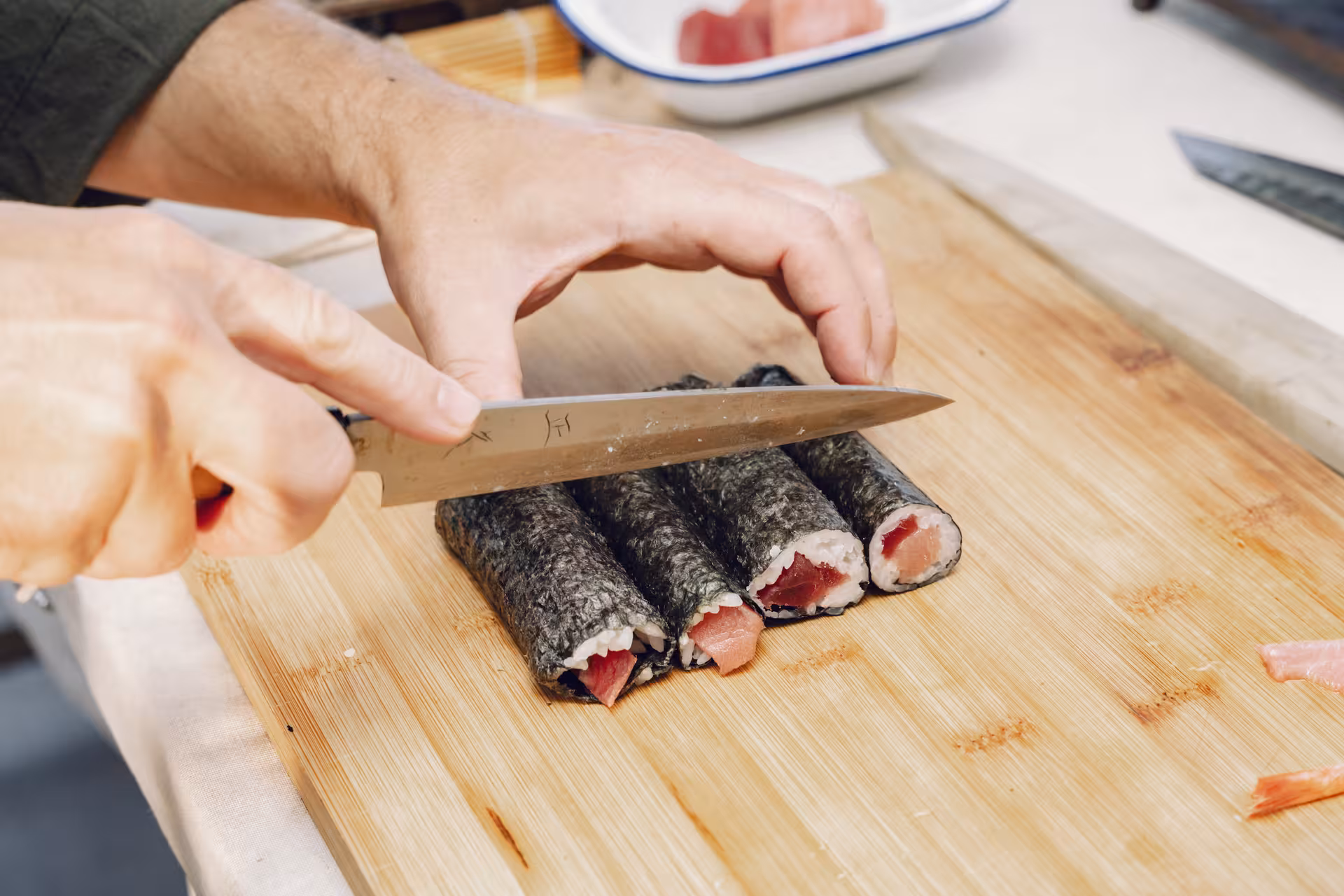 Close-up of cutting nori-wrapped tuna maki rolls on a bamboo board in a hands-on Sushi Masterclass