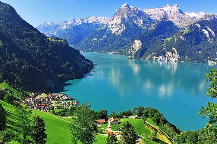 Scenic view of Swiss alpine lake surrounded by lush green hills and snow-capped mountains, perfect for a train tour.