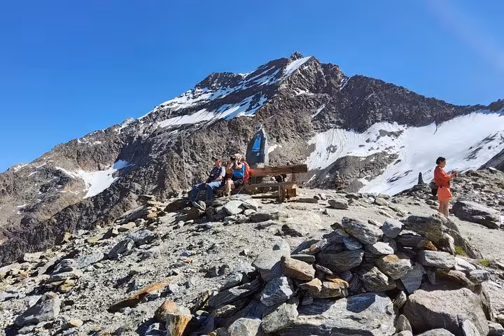 Hikers resting on rocky ridge with snowy Swiss Alps peak backdrop, hidden gems day on Zermatt Jungfrau tour