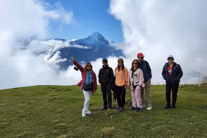 Small group posing on grassy ridge above clouds with snowy peaks, Zermatt and Jungfrau Alps tour